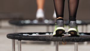 Nahaufnahme von Füßen in Sportschuhen, die auf einem Minitrampolin springen; im Hintergrund sind weitere Trampoline unscharf zu erkennen