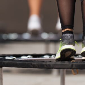 Nahaufnahme von Füßen in Sportschuhen, die auf einem Minitrampolin springen; im Hintergrund sind weitere Trampoline unscharf zu erkennen
